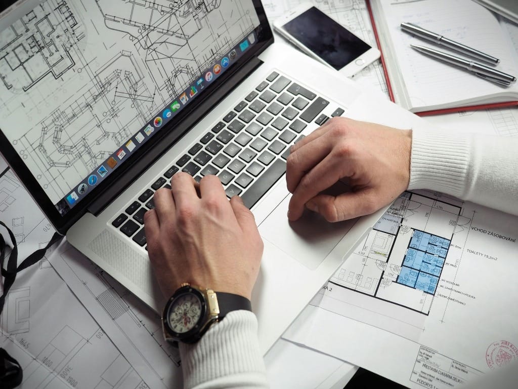 Hands working on architectural design plans on a laptop for a project in Milton Keynes.